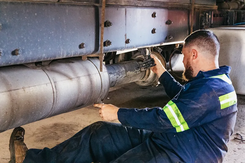 After treatment system repair beneath a heavy-duty truck, with a technician servicing the exhaust components.