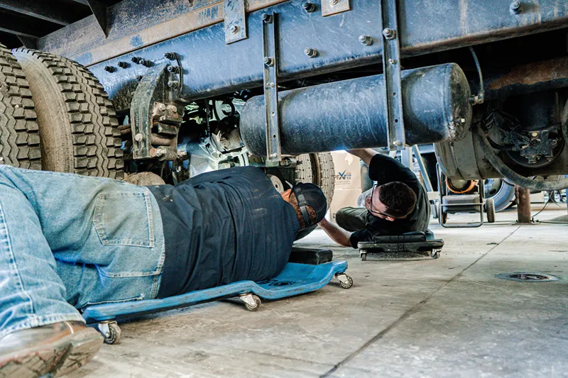 EGR and DPF service performed beneath a heavy-duty truck by technicians inspecting emissions system components.
