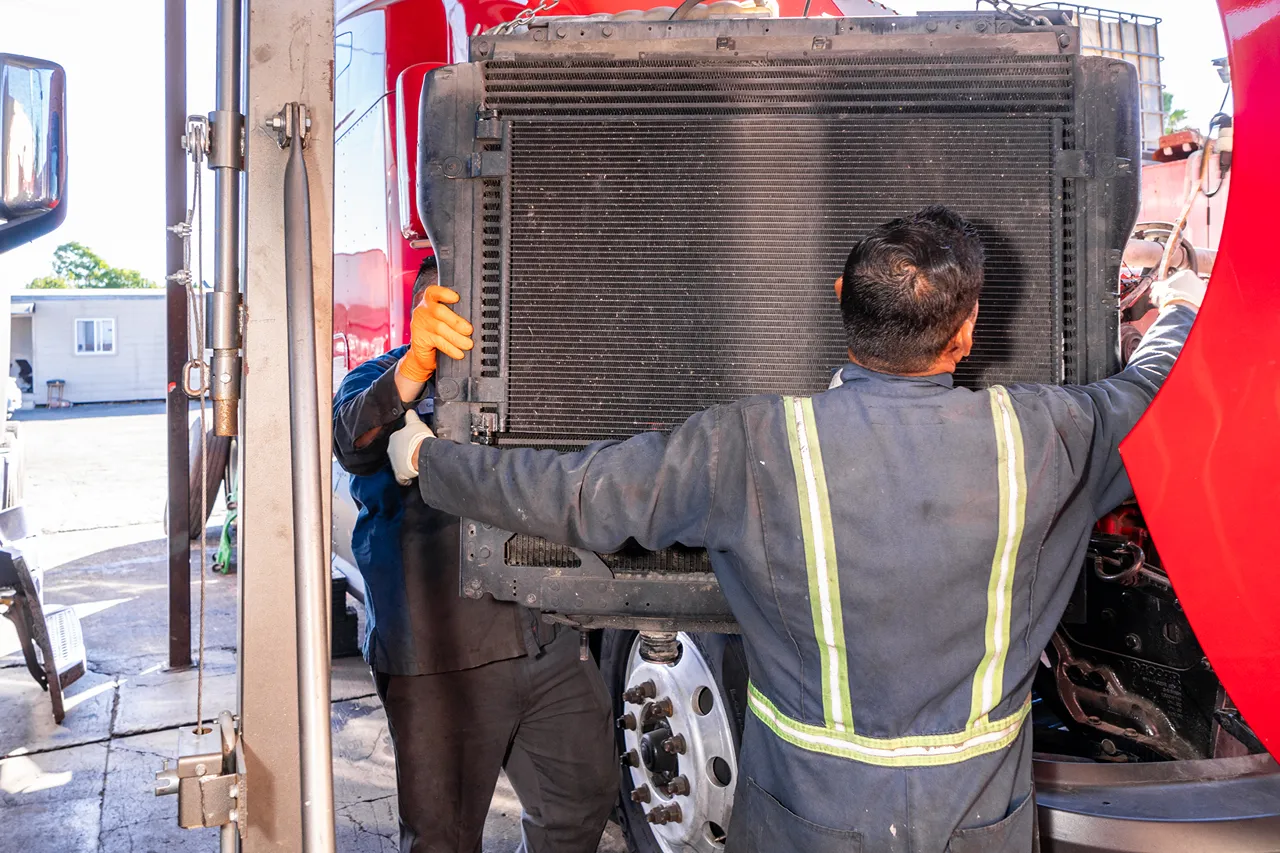 Coolant systems service as technicians remove a large radiator from a heavy-duty truck for repair.