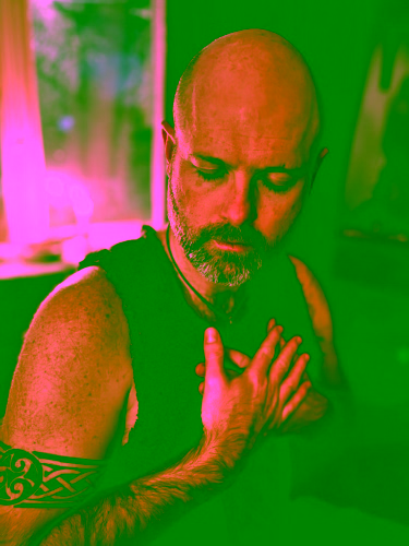 Man practicing ancestral healing meditation indoors, eyes closed with hands over heart, wearing a textured vest in a warm candlelit space, conveying mindfulness, grounding, and spiritual reflection.