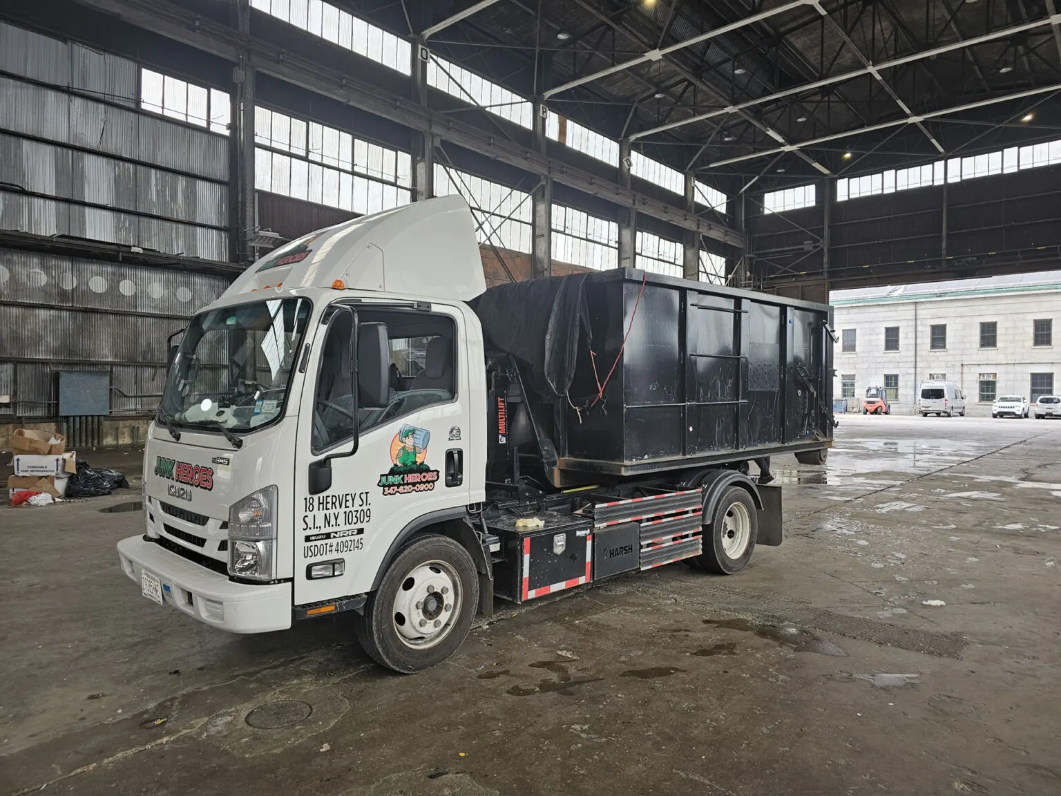 A Junk Heroes truck with a roll-off container parked inside a warehouse