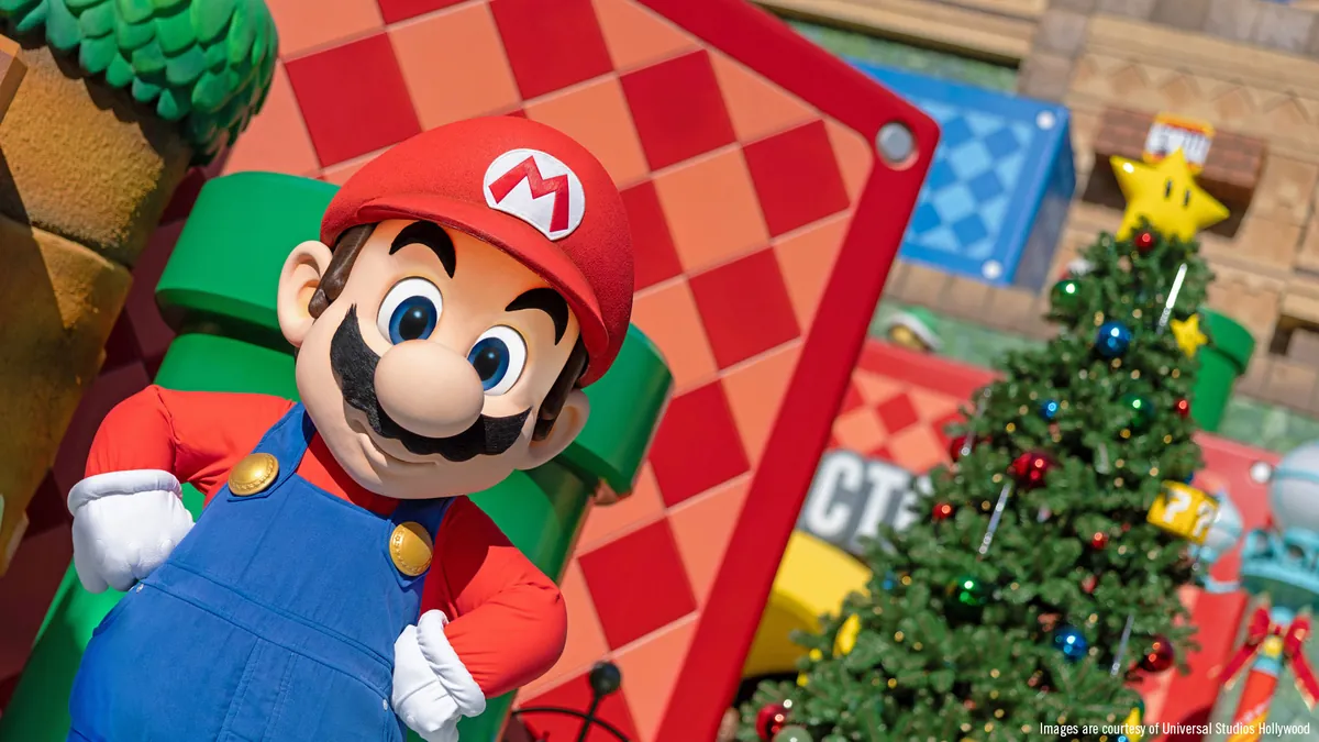 Mario beside a decorated Christmas tree in Super Nintendo World during the holidays.