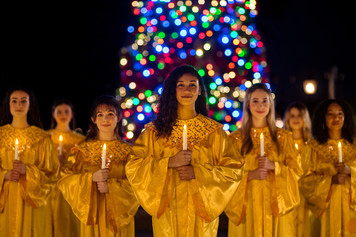 Candlelight Processional choir in gold robes holding candles in front of a Christmas tree at Epcot