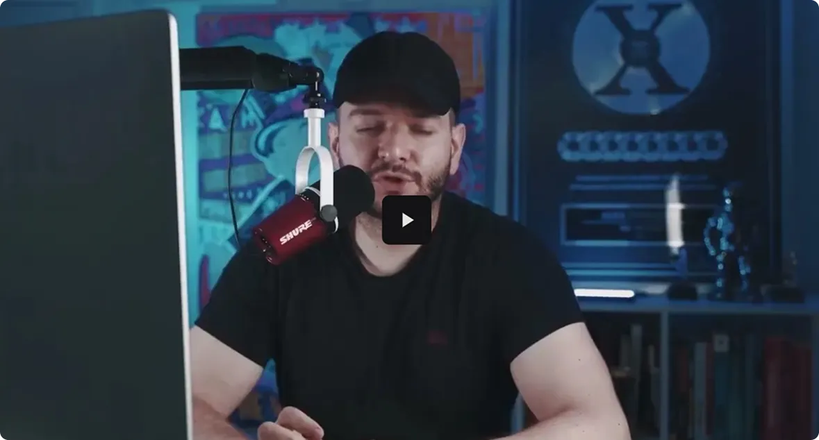 A person wearing a black cap sits in front of a microphone, discussing topics with artistic backgrounds and shelves behind them.