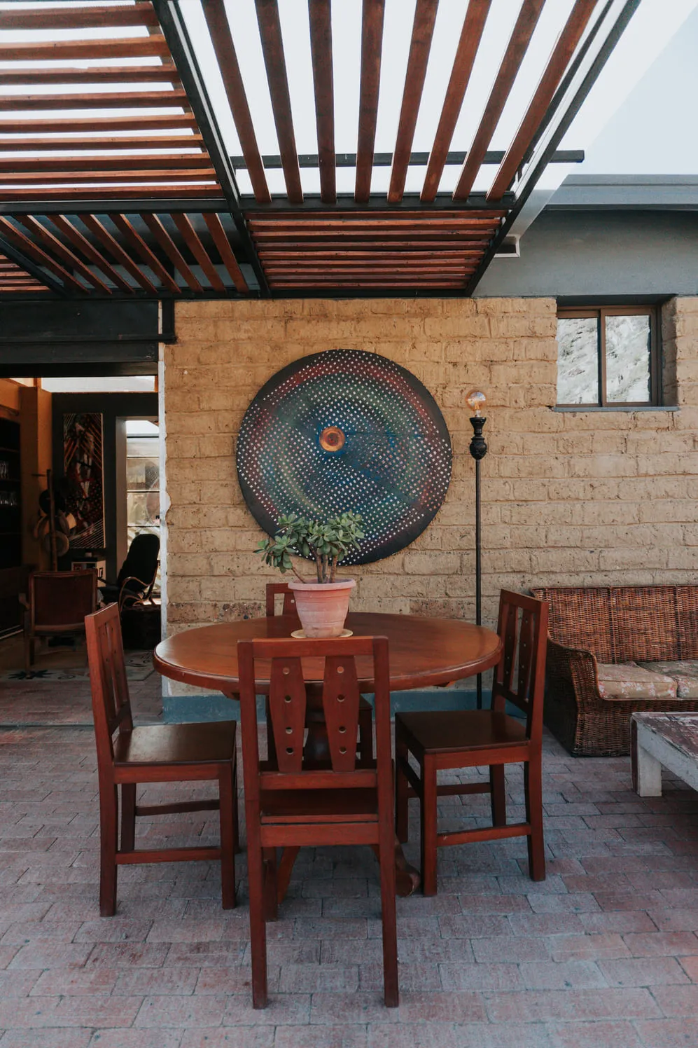 Mesa de comedor con sillas en el patio, frente a un muro con un mosaico circular.