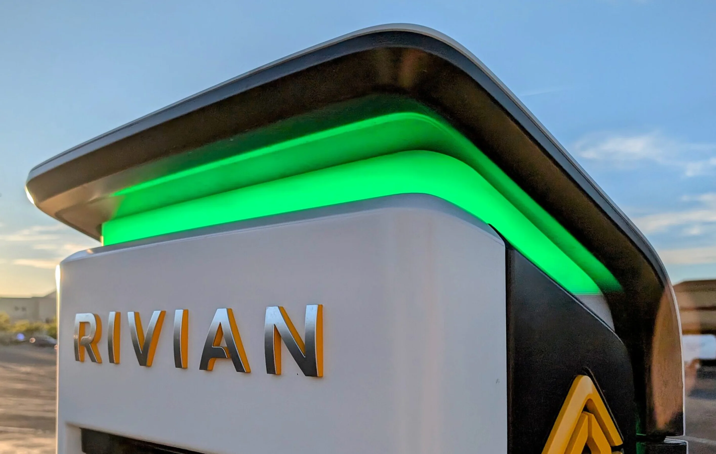 A Rivian charger at sunset, its canopy lit by an Energy green light bar