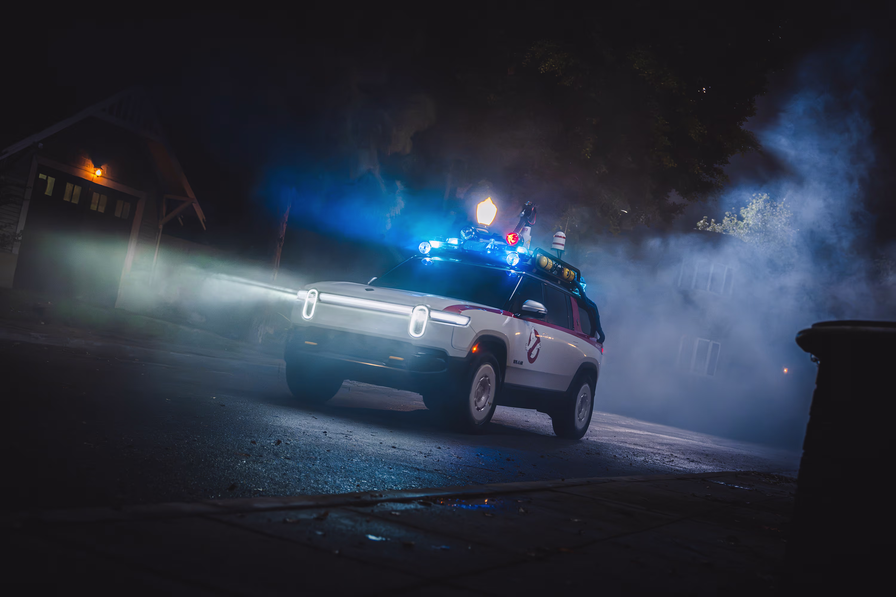 The Ghostbusters R1S driving through fog at night, headlights and blue roof lights on.