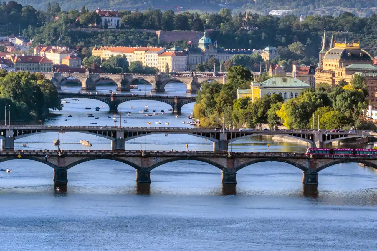 Panoramatický pohled na pražské mosty přes Vltavu – Palackého, Jiráskův, Legií a Karlův most s Národním divadlem v pozadí.