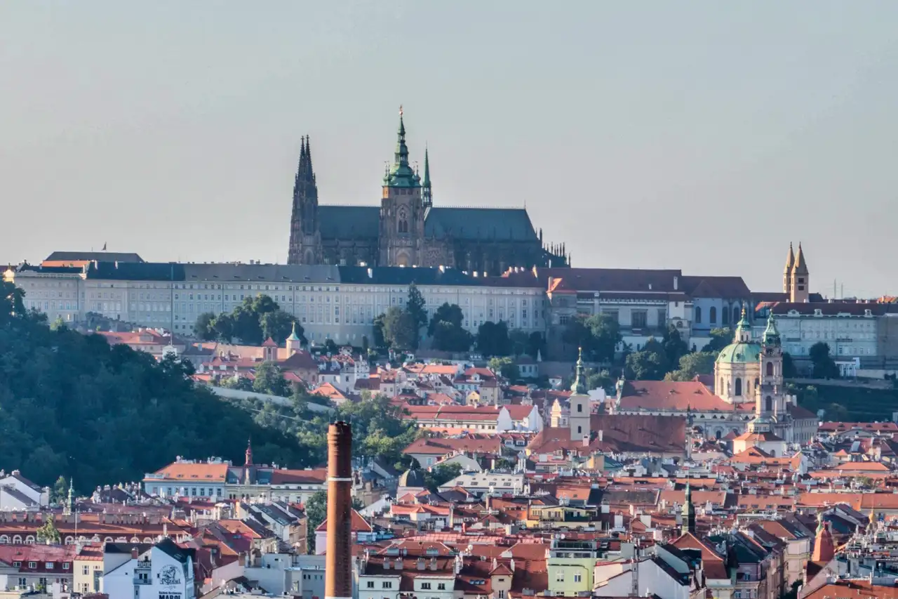 Pohled na Pražský hrad a katedrálu sv. Víta přes červené střechy Malé Strany za letního podvečera.