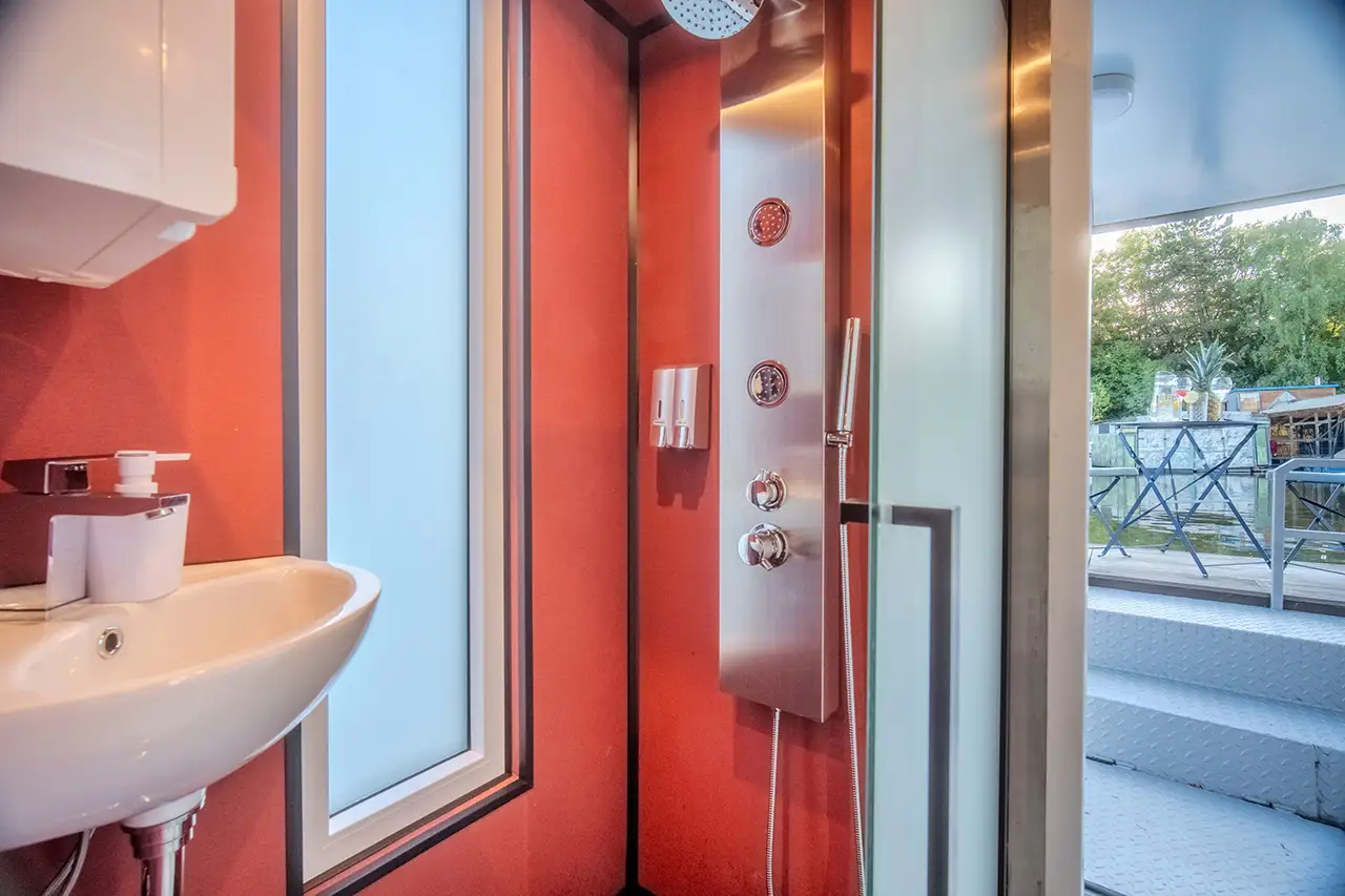 oderní koupelna houseboatu Neptun – sprchový panel s dešťovou hlavicí, umyvadlo a skleněné dveře s výhledem na palubu.