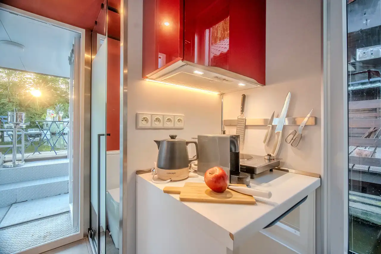 uchyňka houseboatu Neptun v detailu – rychlovarná konvice, kávovar, prkénko a magnetický držák nožů pod červenými horními skříňkami.