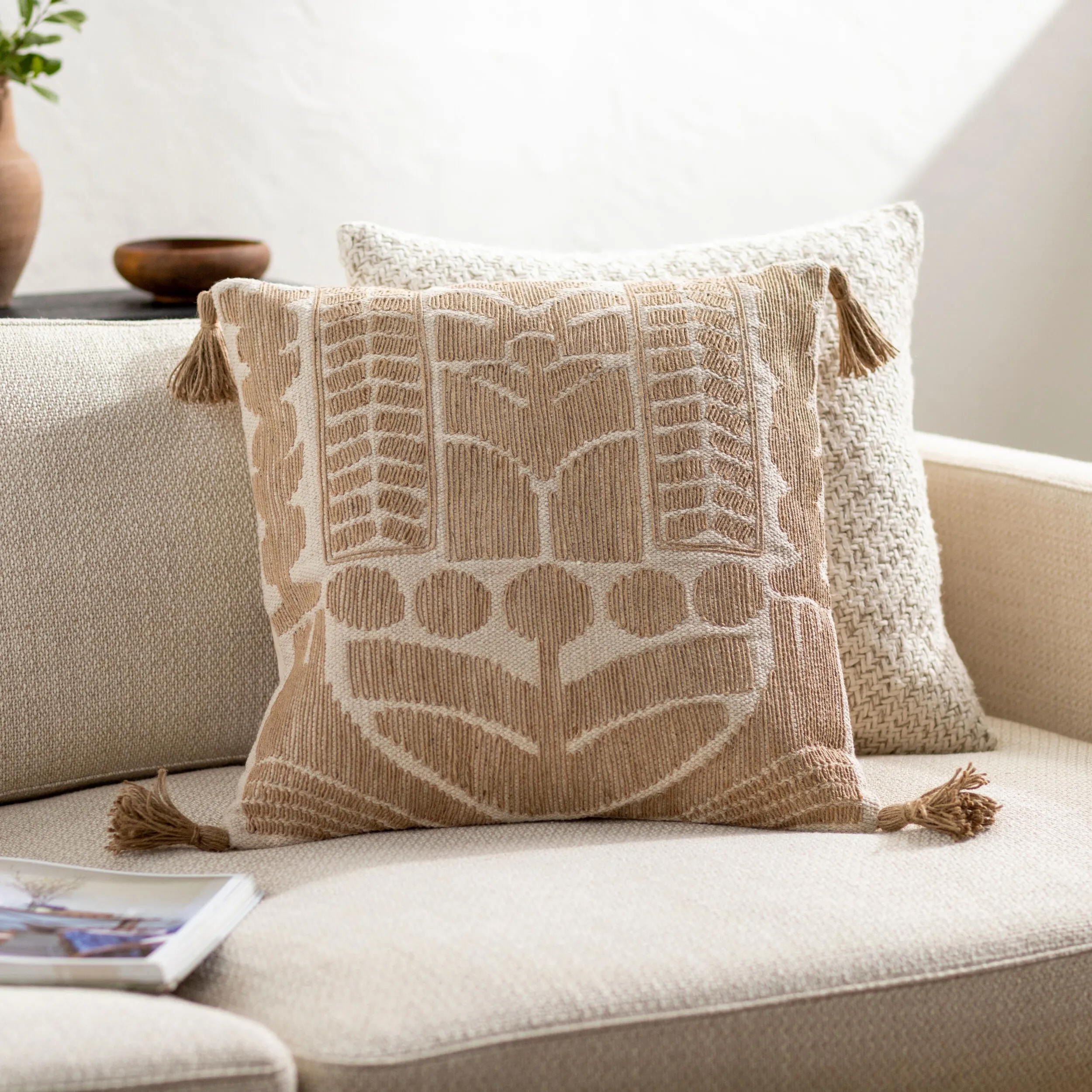 Light brown and white patterned pillow with dark brown tassels on the ends sitting on a white sofa