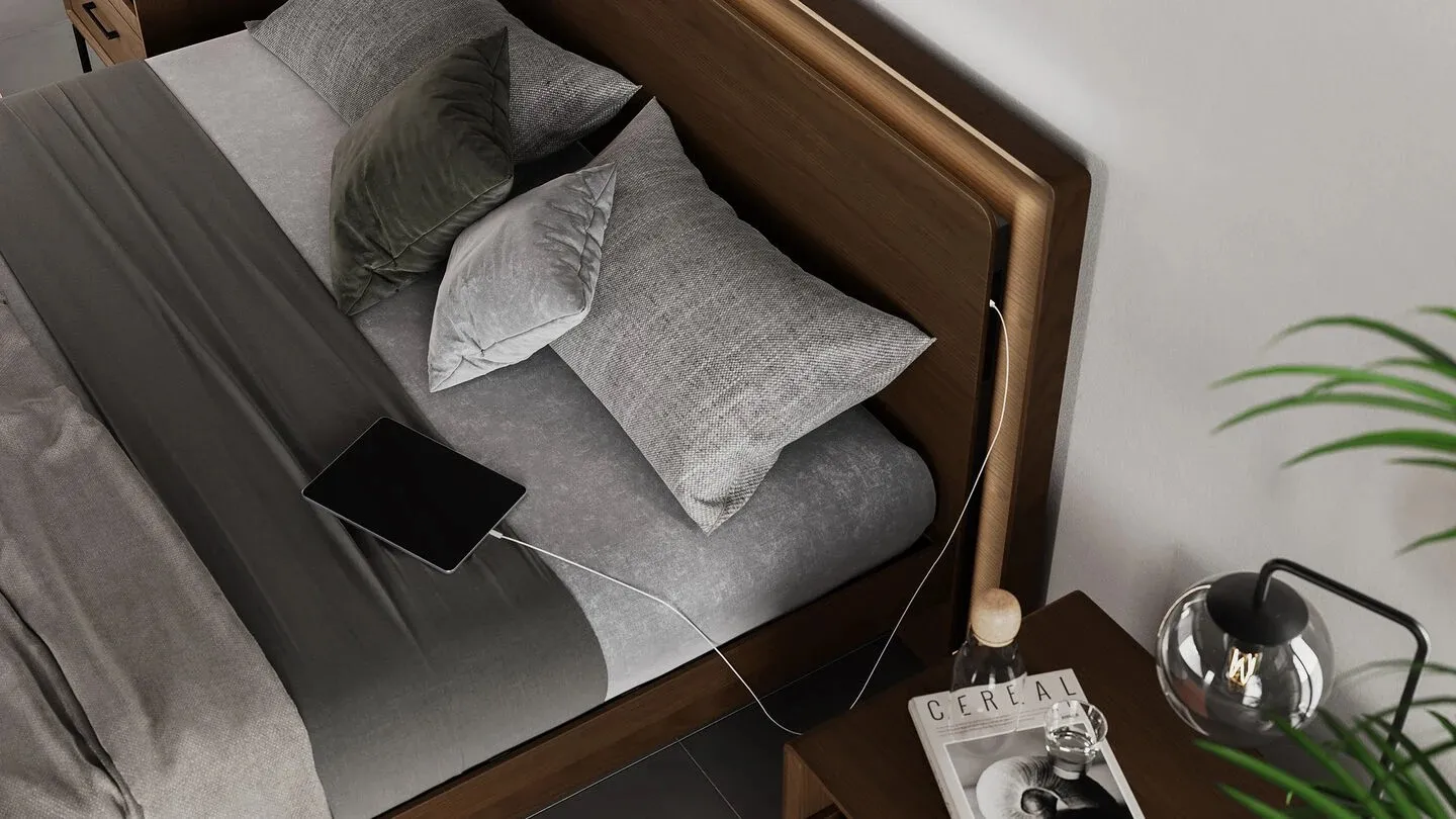 A brown headboard with built in phone charger and bed with grey sheets and grey pillows