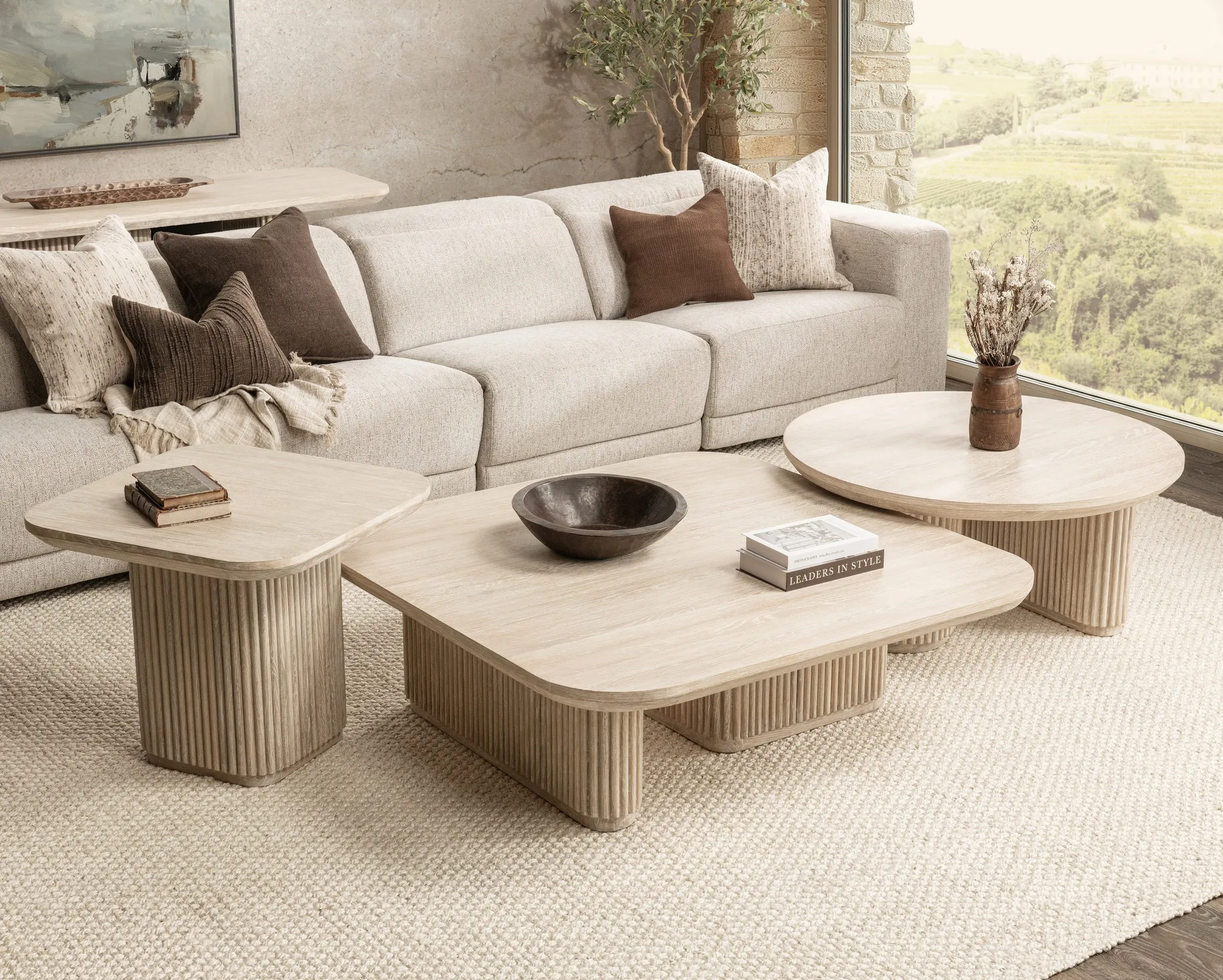 White sofa in living room with two brown pillows and two white pillows, and three beige coffee tables 
