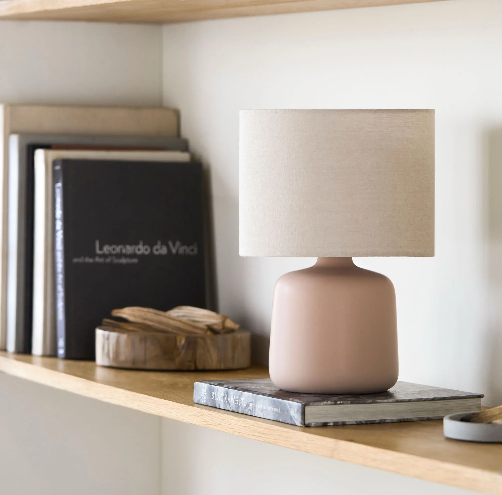 Light pink table lamp sitting on top of a book which is sitting on top of a shelf