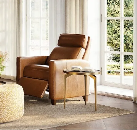 Brown leather recliner next to brightly lit square window with green trees outside