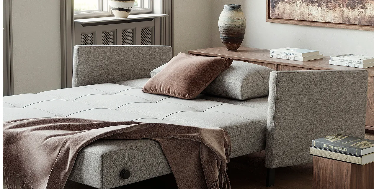 White sleeper sofa with brown throw blanket and brown pillow