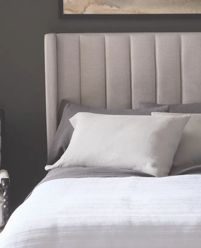 Two white pillows with tall beige headboard and white comforter 