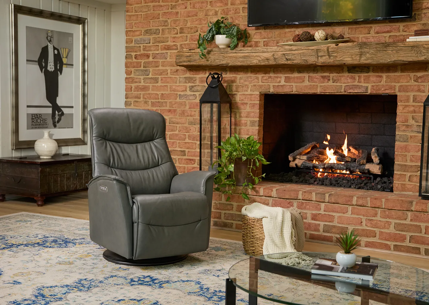 A dark grey leather recliner next to a burning fireplace with a white and blue rug