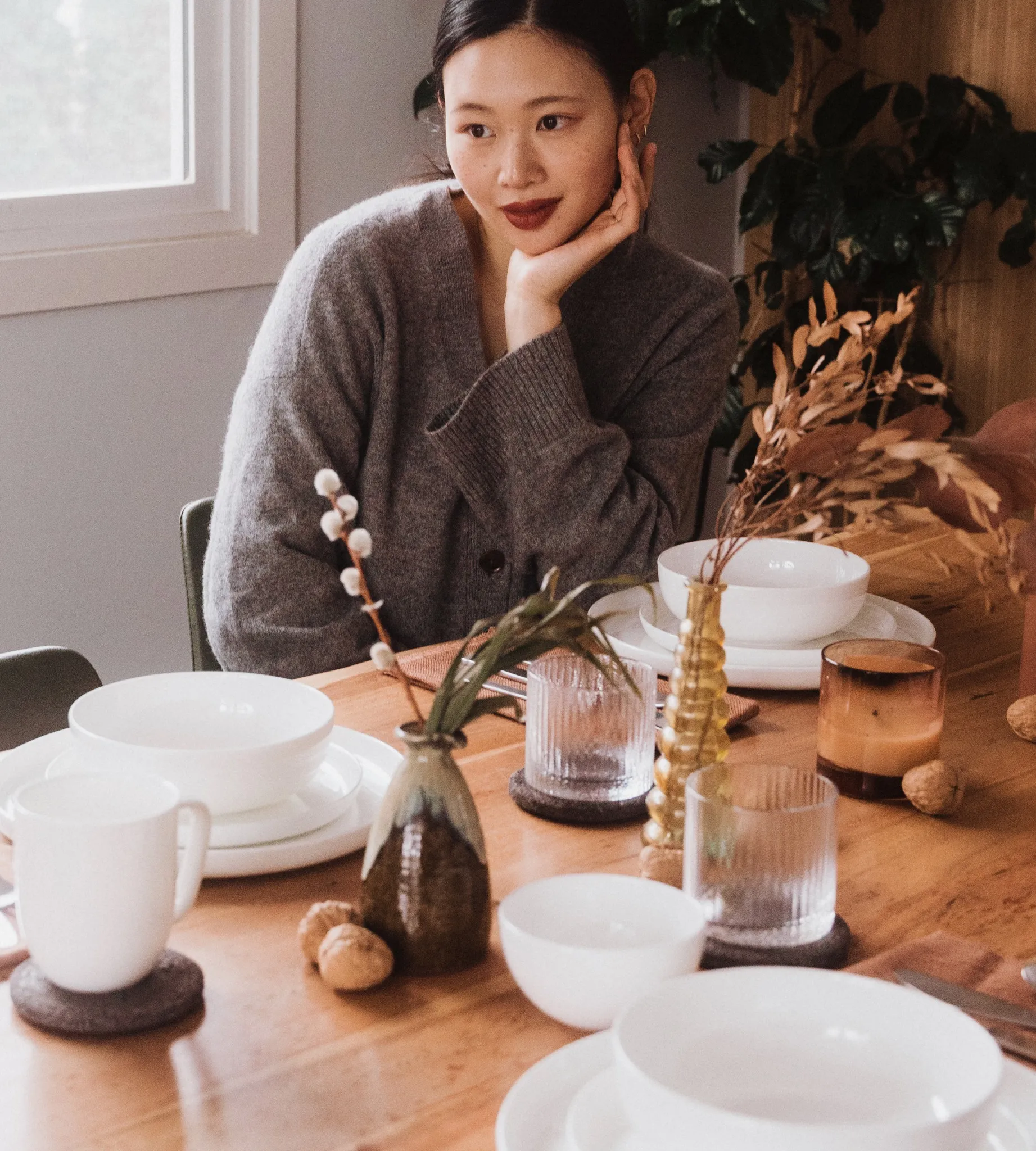Woman model with hand sitting on chin sitting at dining table full of plates and cups smiling