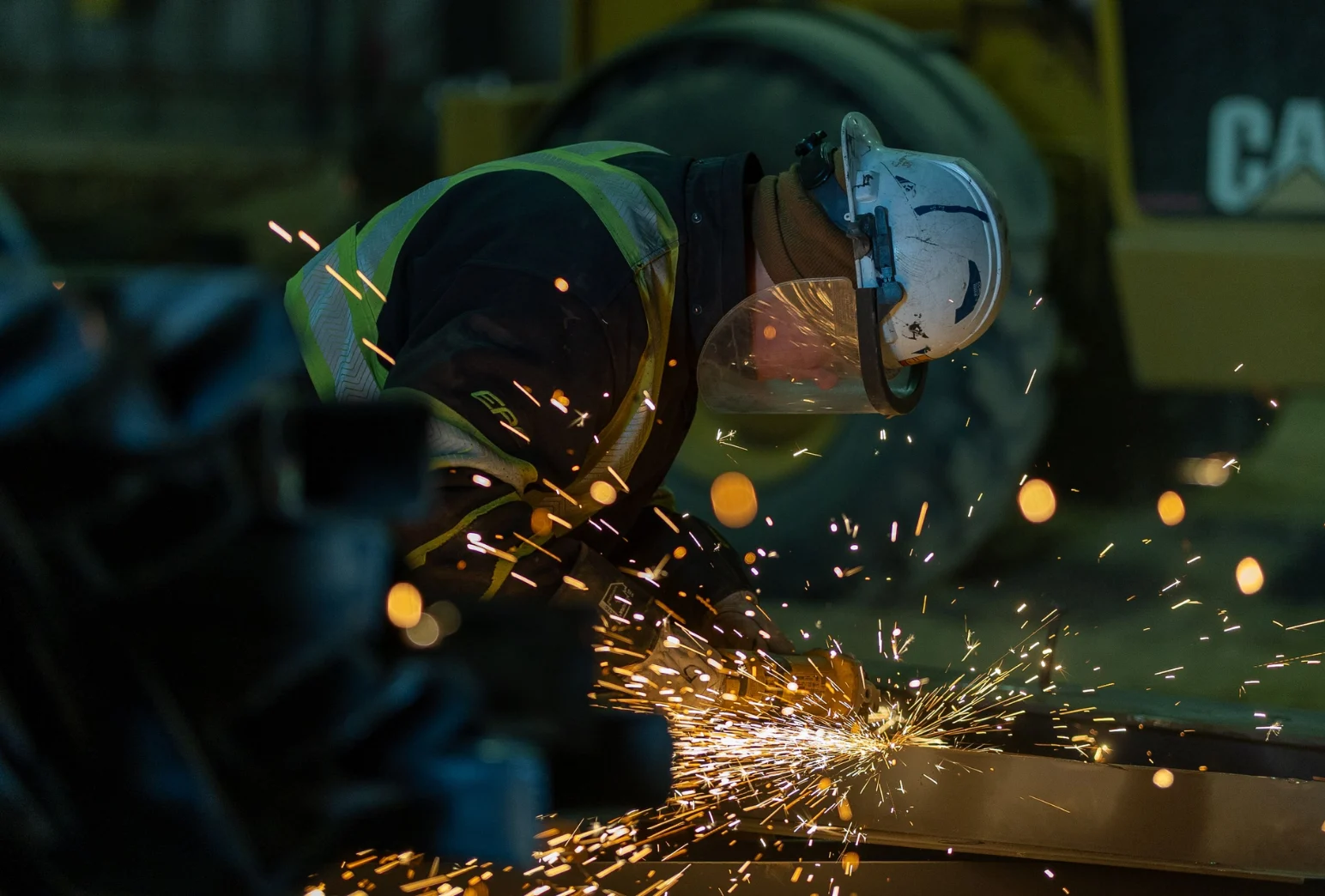 Construction worker using angle grinder cutting metal with sparks on Edmonton jobsite