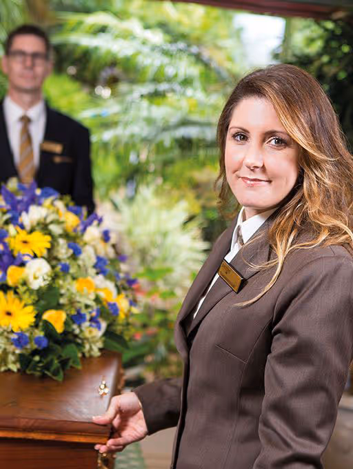 A female funeral director stands by a coffin.