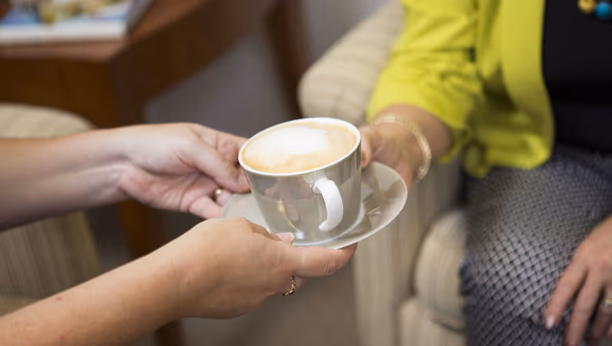 Hands offering a cup of coffee to someone.