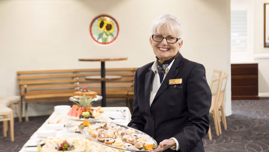 A smiling woman holds a tray of pastries.