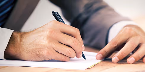Close-up of a man's hand writing on paper.
