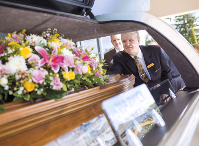 Casket with flowers in a hearse, two men.