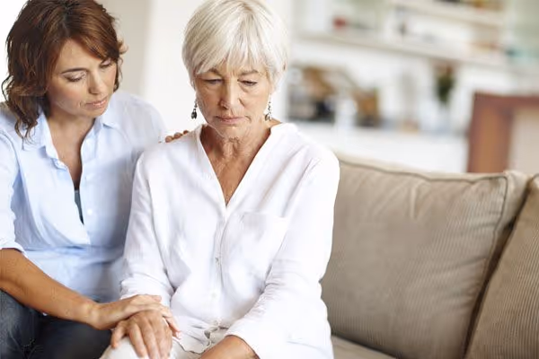 A younger woman consoles an older, sad woman on a couch.