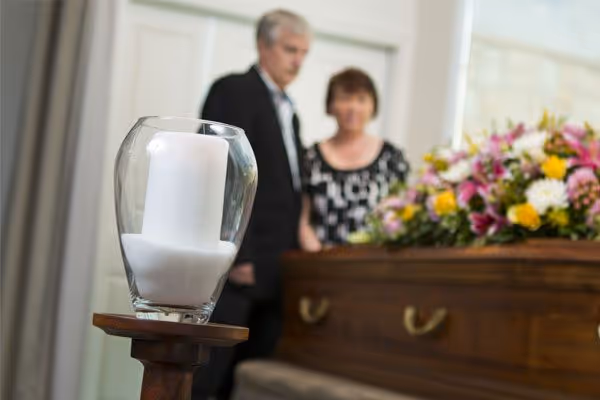 A memorial candle in the foreground, with a couple and casket blurred.