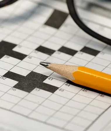 A sharpened pencil resting on a partially completed crossword puzzle.