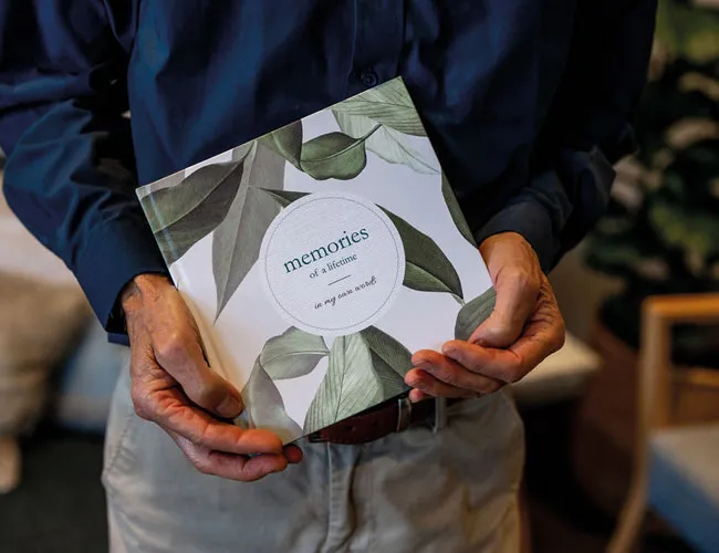 Man holding a "memories of a lifetime" book with green leaves design.
