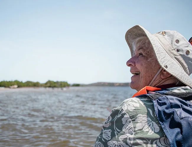 Smiling older woman in hat and life vest on a boat.