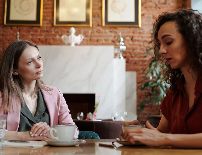 Two women seated at a table, one listening, one speaking.
