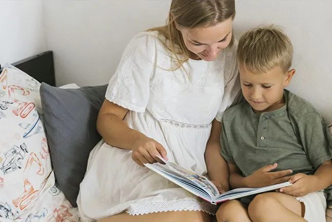 A smiling mother reads a book to her young son.