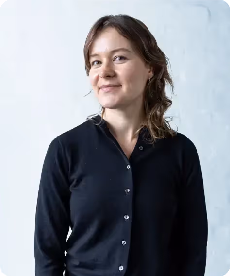 Smiling woman with wavy brown hair wearing a black buttoned cardigan against a light background.