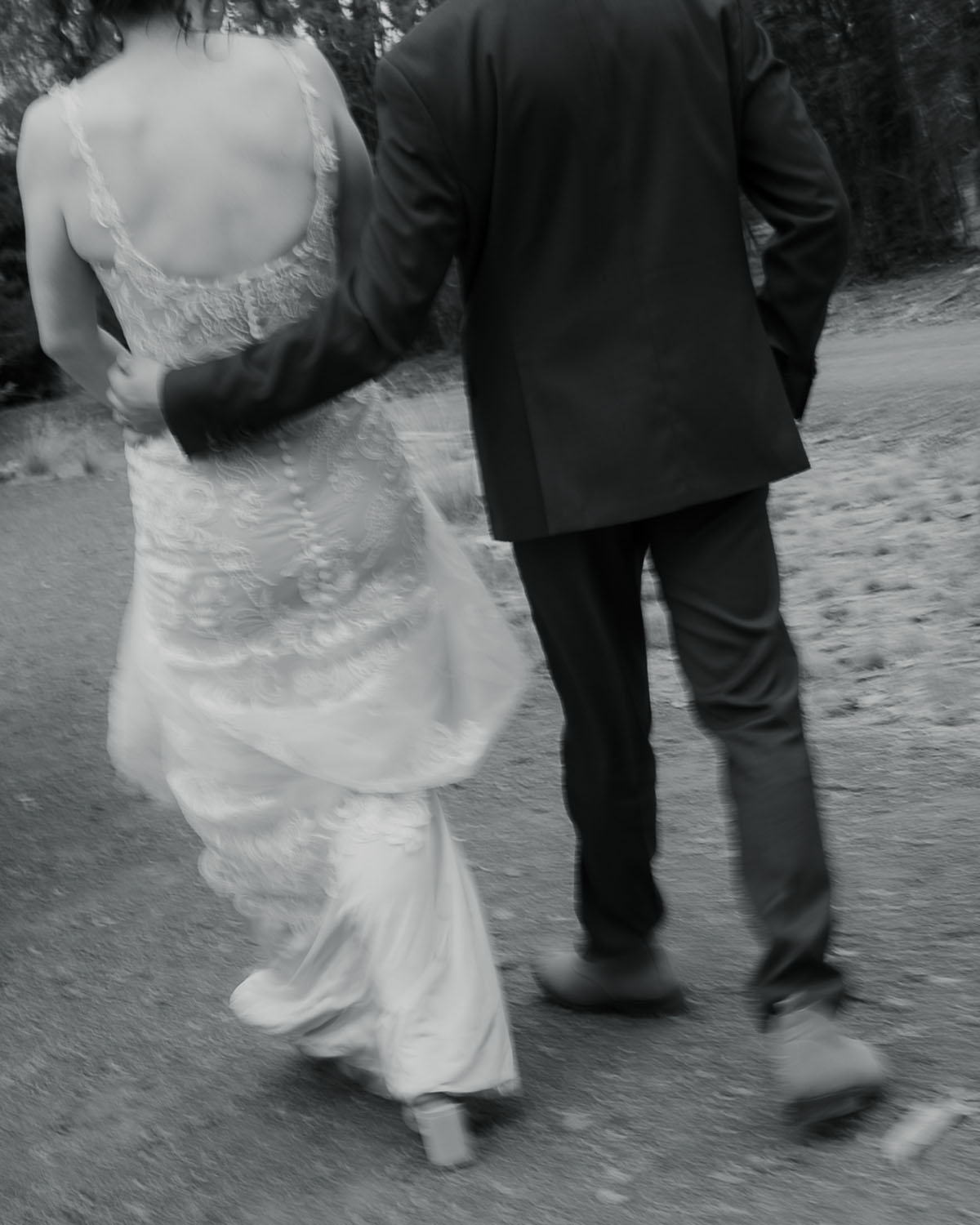 Couple walking hand in hand outdoors, the woman in a lace wedding dress and the man in a dark suit.