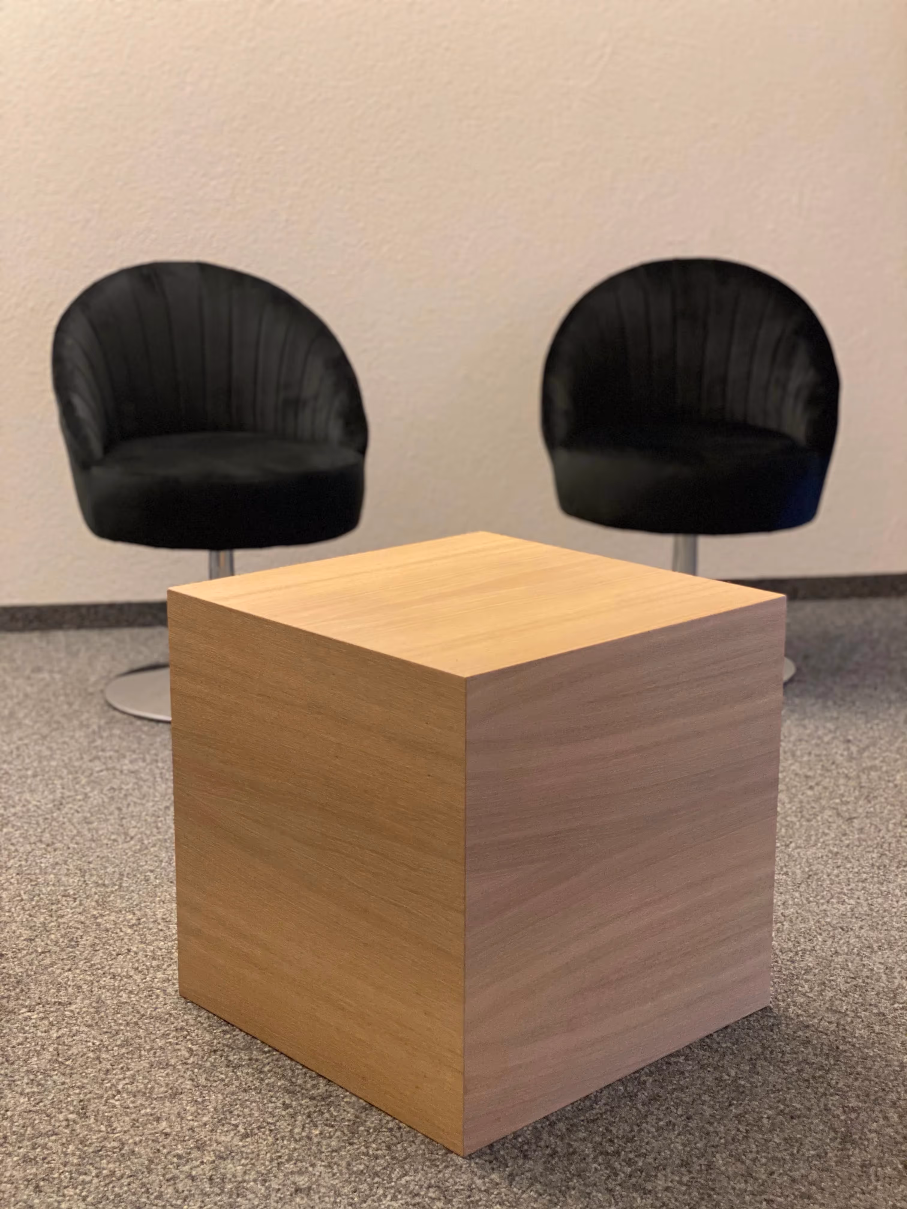 Zwei schwarze Stühle und ein hölzerner Würfel auf grauem Teppich