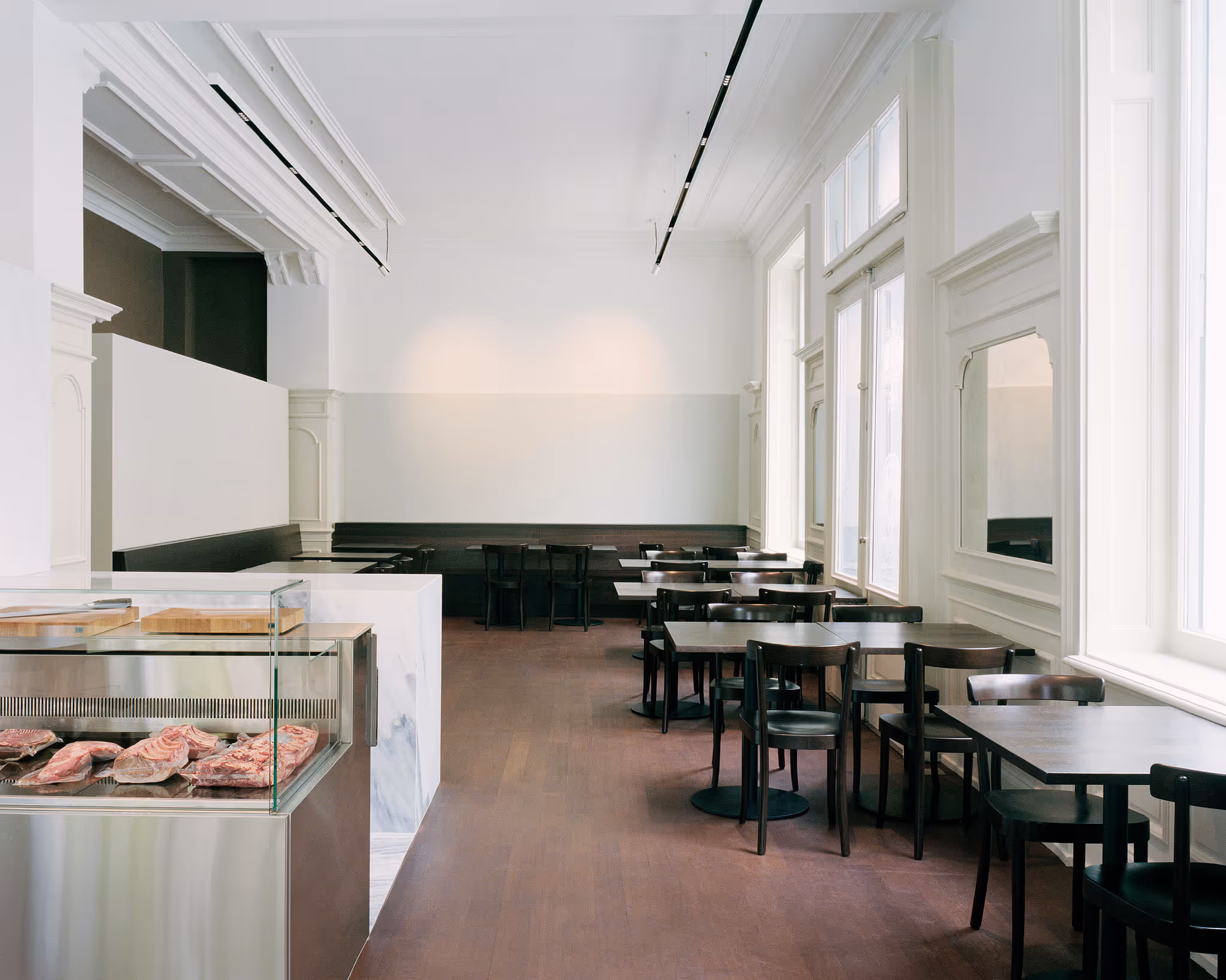 Modernes Restaurant mit weißen Wänden, schwarzen Tischen und Fleischtheke