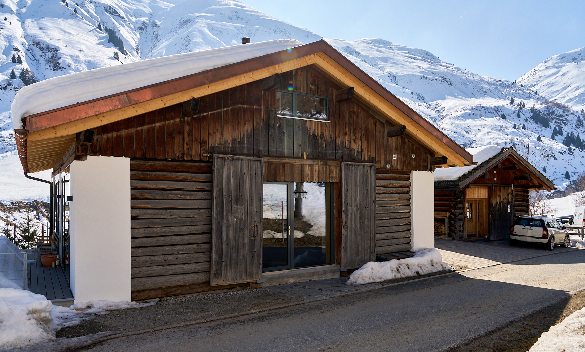 Holzhütte in verschneiter Berglandschaft mit Parkplatz und Winterkulisse