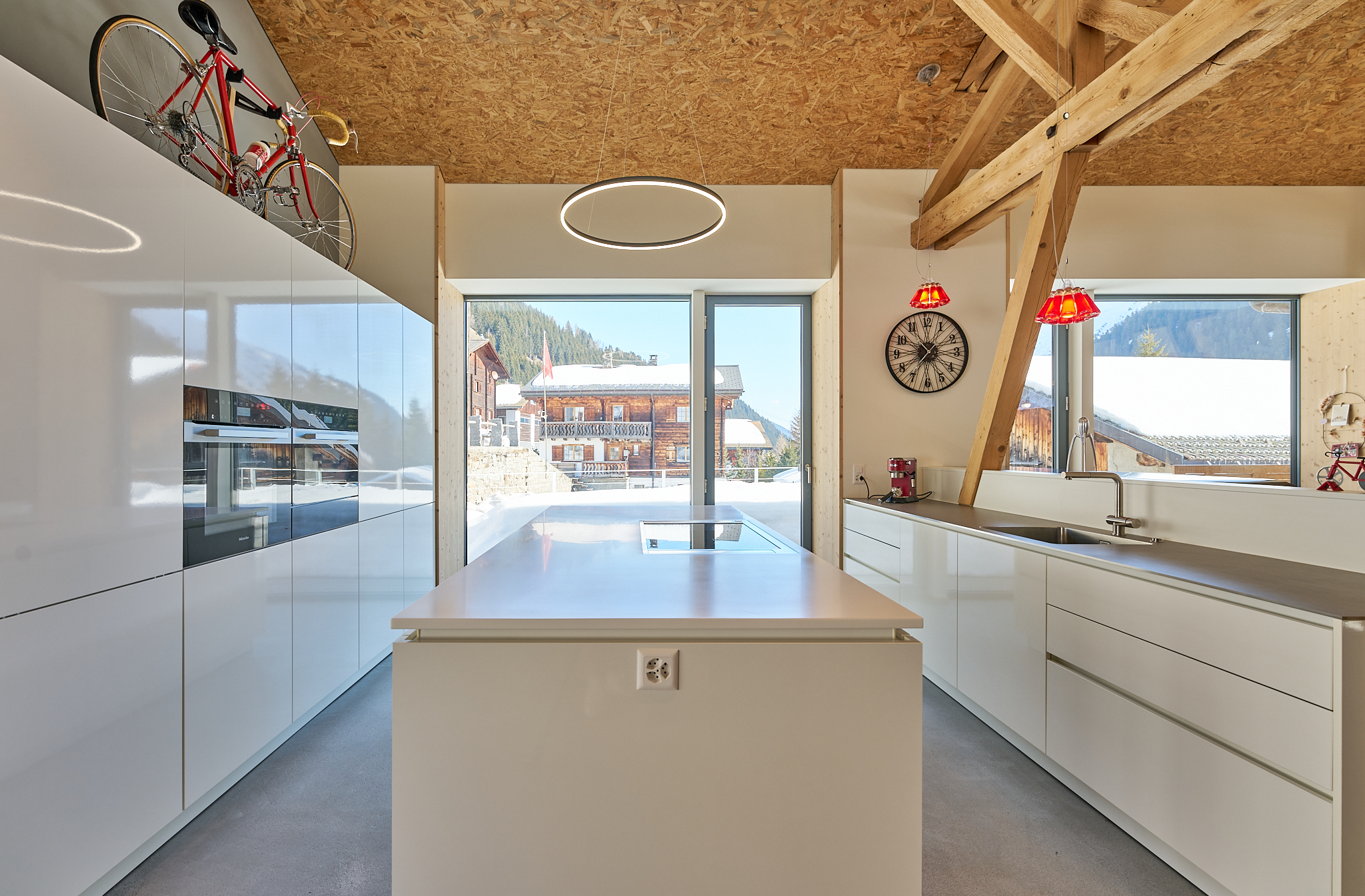Moderne, weiße Küche mit Fahrrad und Bergblick durch große Fenster