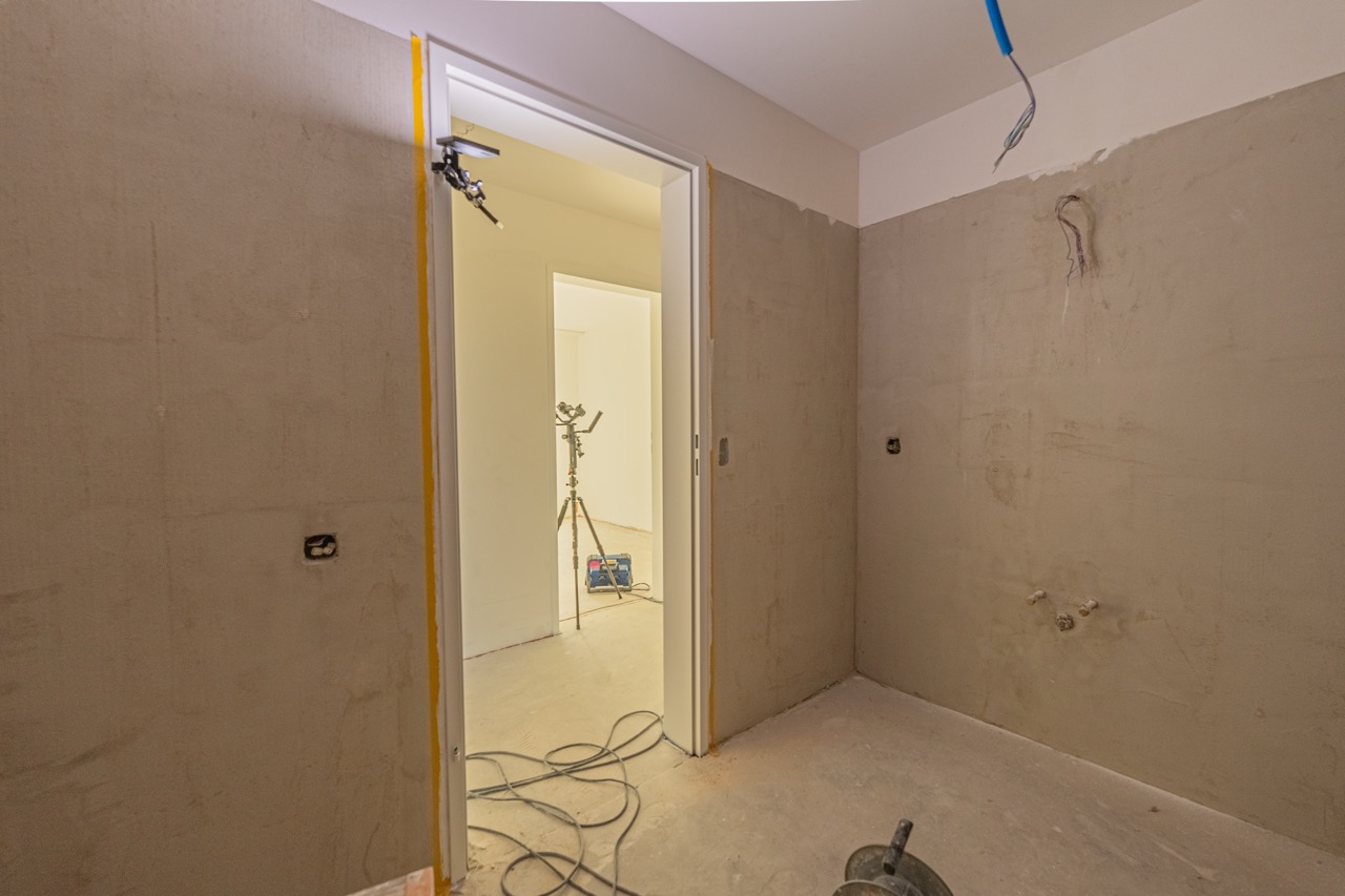 Rohbau einer Wohnung mit Tür, Kabel und Stativ im Hintergrund