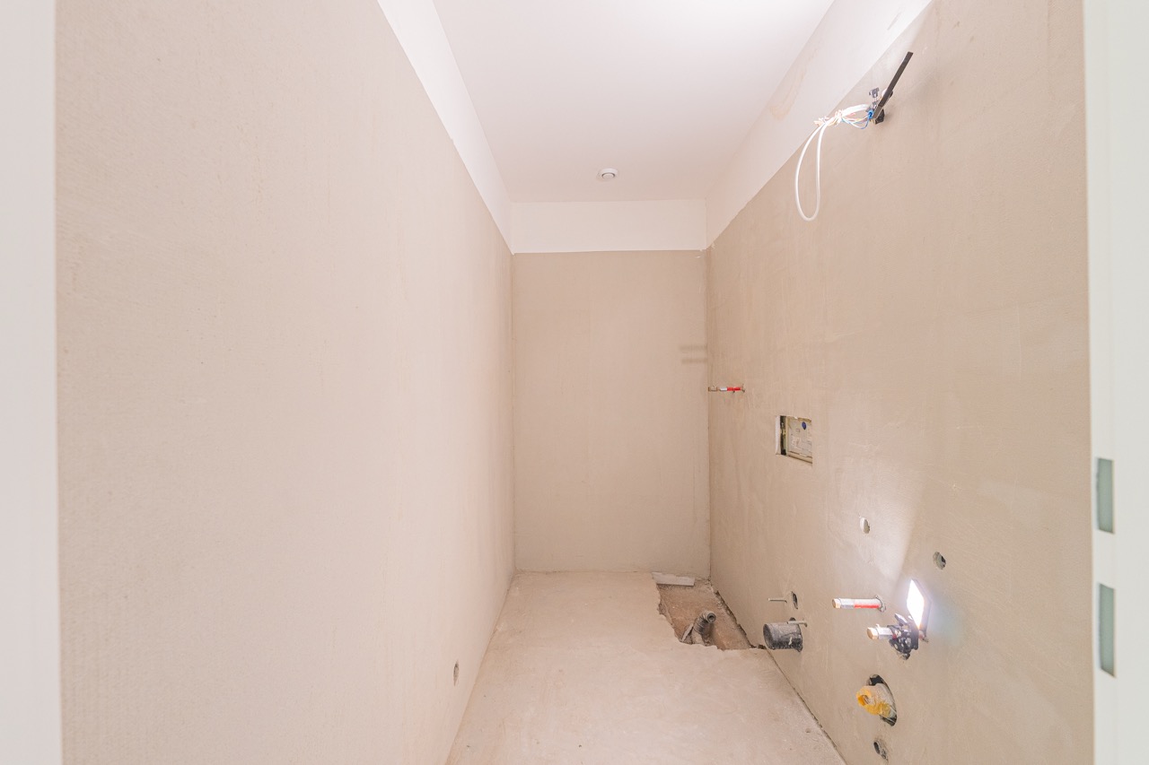 Unfertiges Badezimmer mit Rohinstallationen und beigen Wänden während der Renovierung
