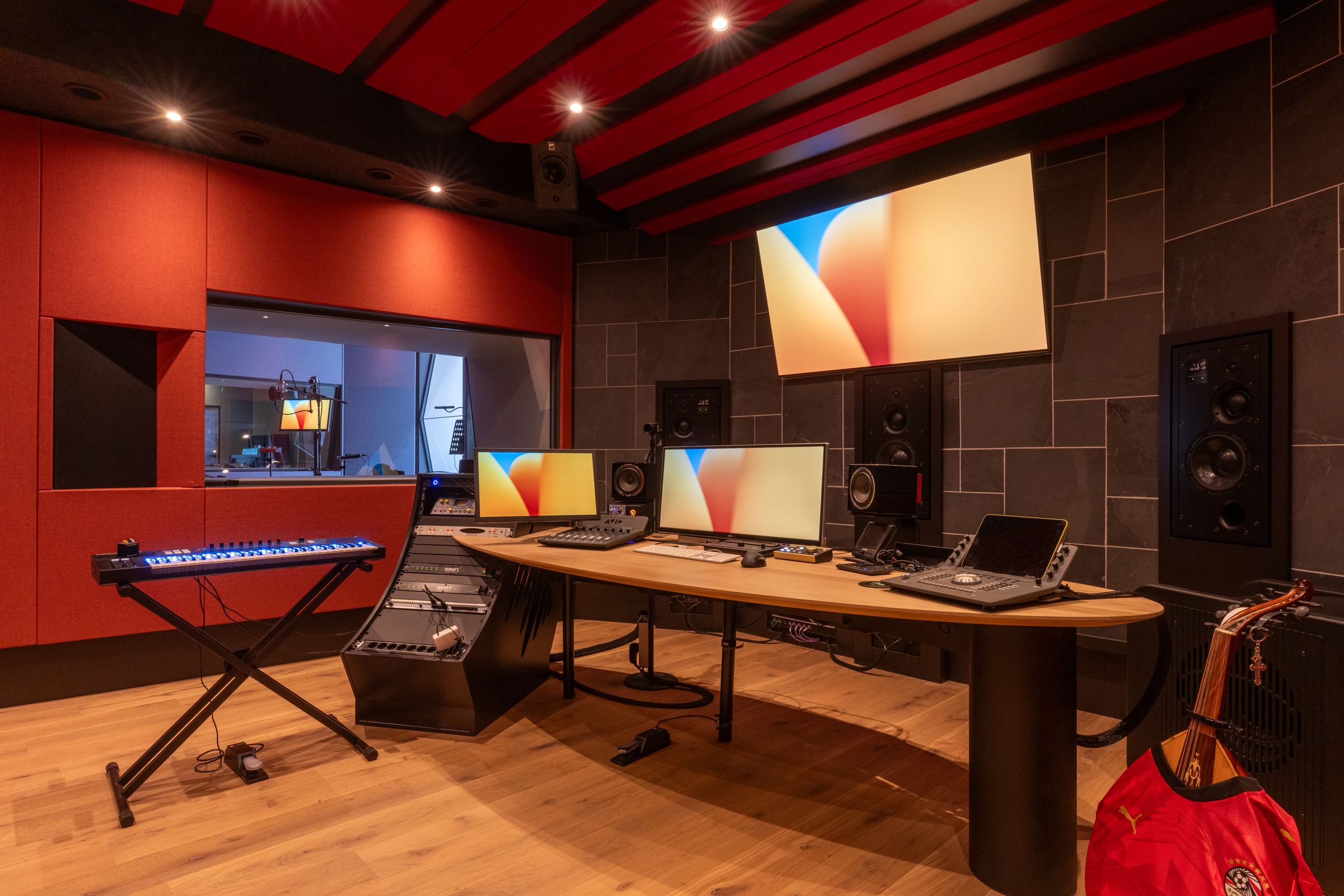 Studio van TFA met rode wanden, een houten regietafel, keyboard en studiomonitoren