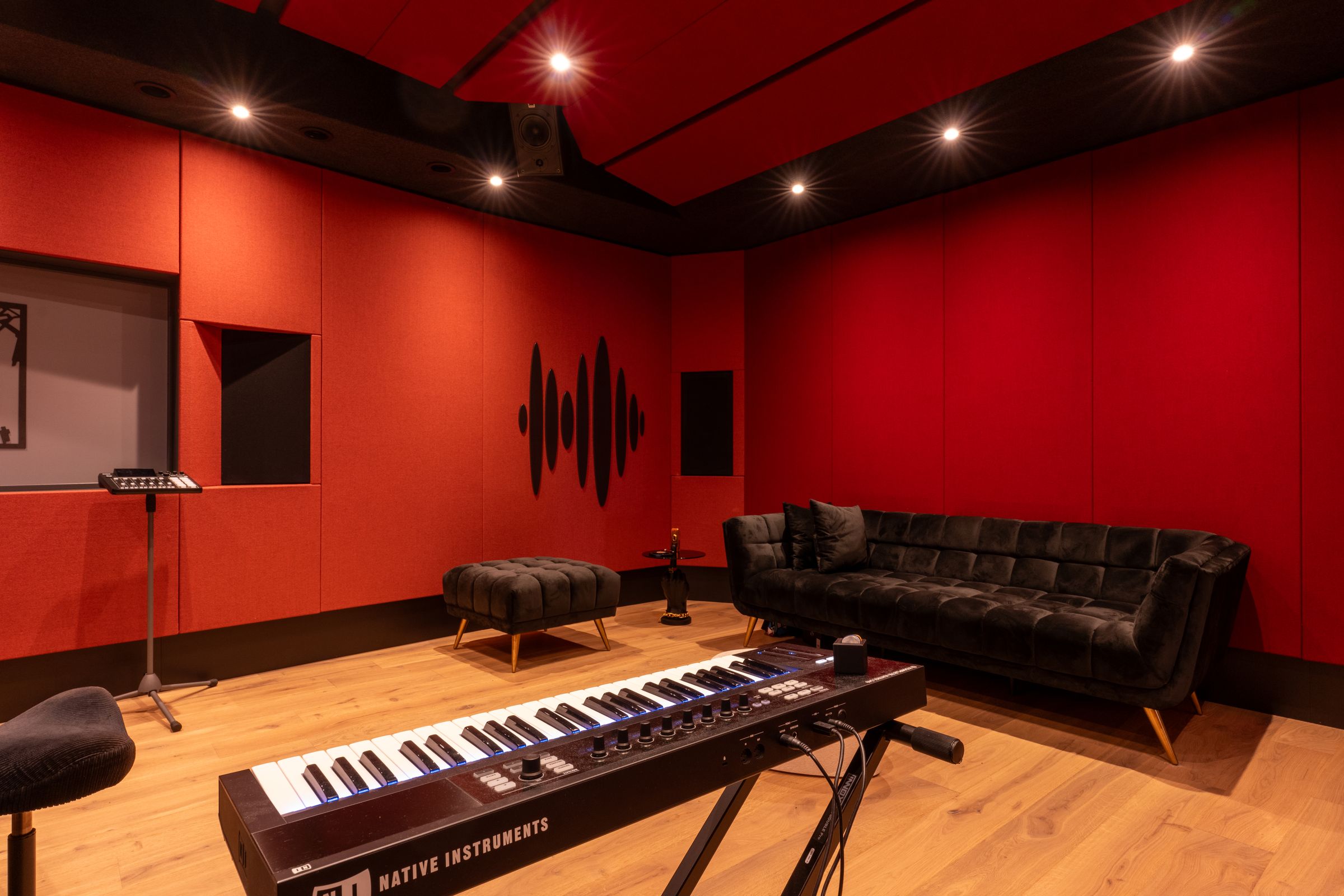 Studio van TFA met rode wanden, een zwarte bank, een keyboard en een akoestisch plafond