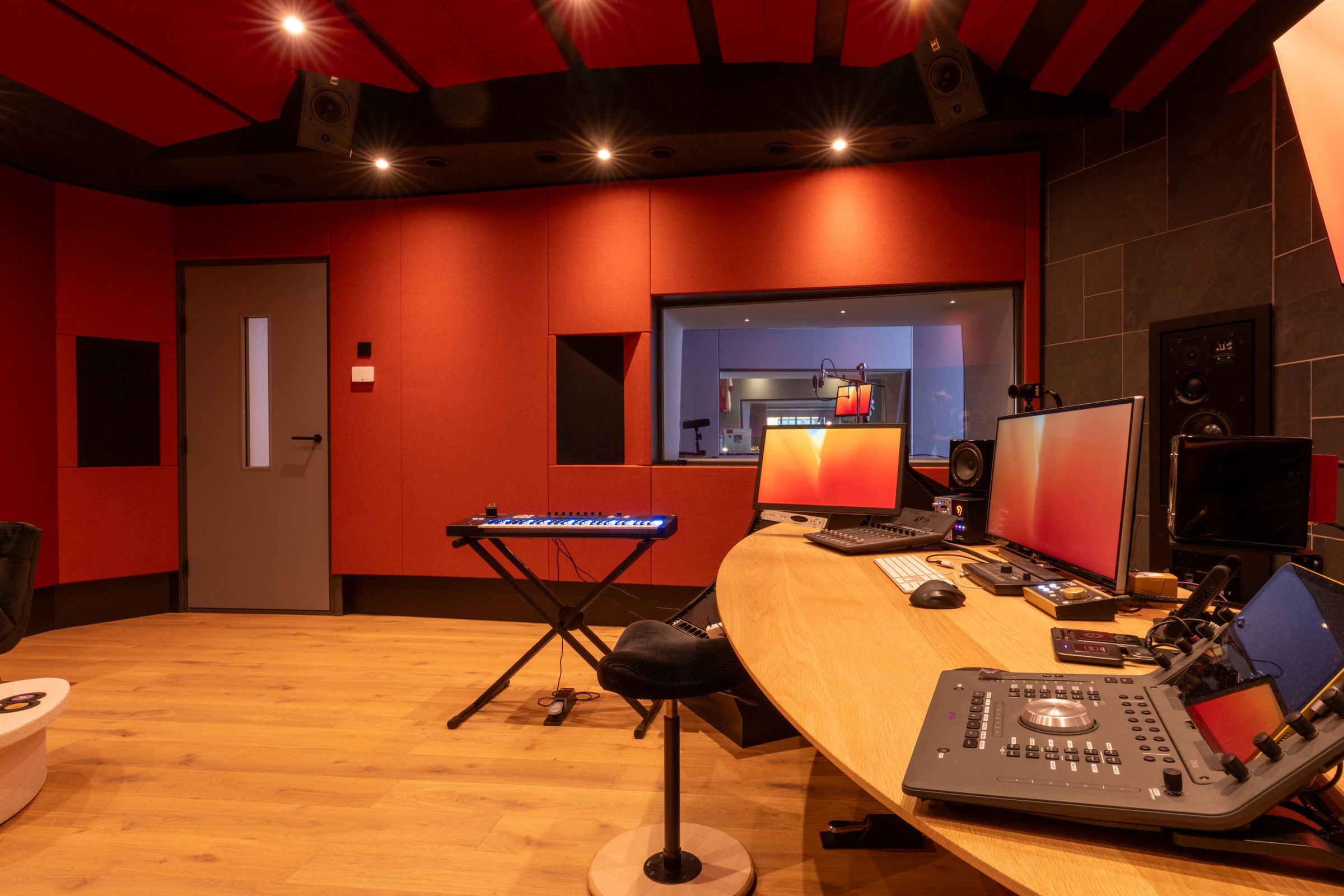 Studio van TFA met rode wanden, een houten regietafel, keyboard en studiomonitoren
