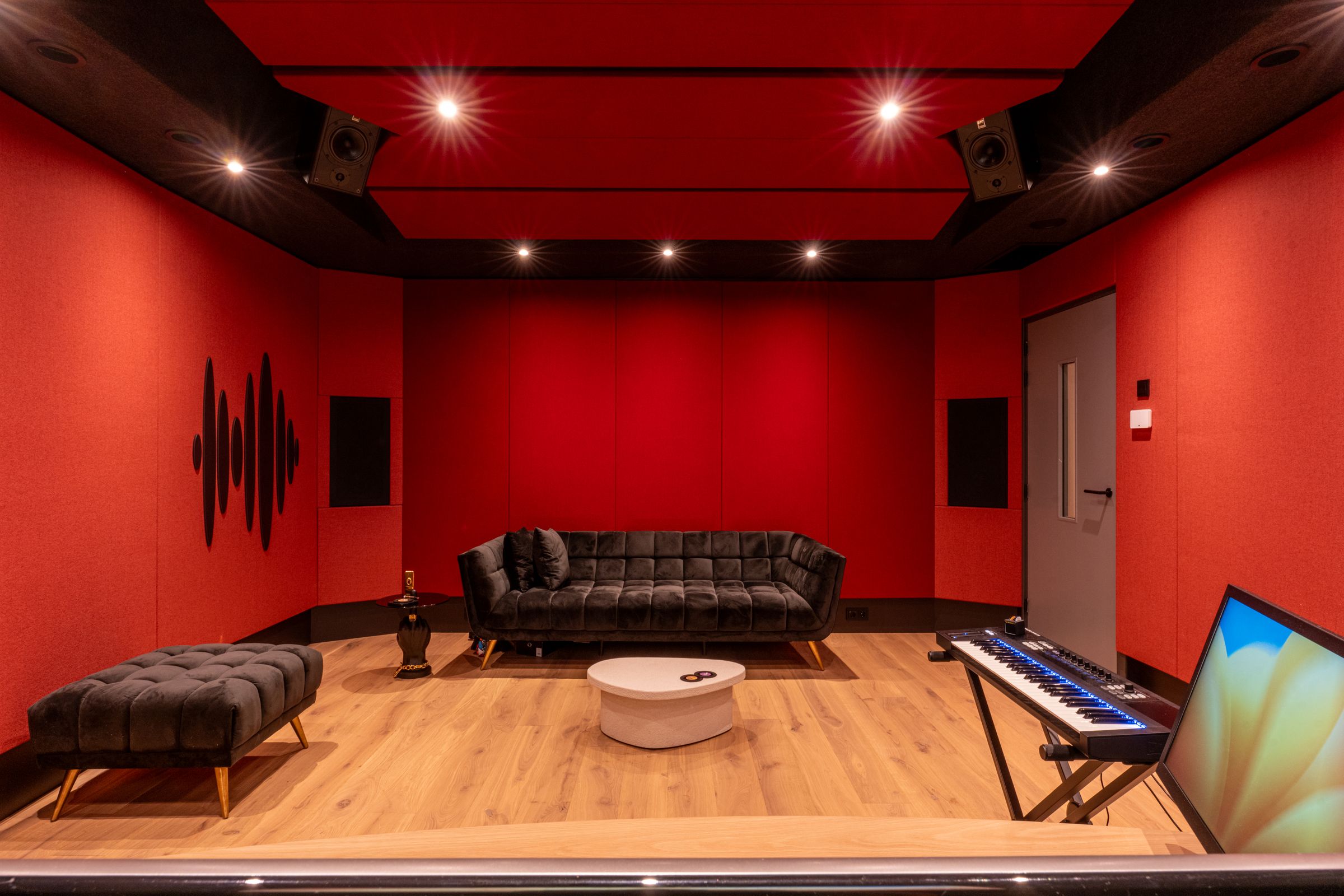 Studio van TFA met rode wanden, een zwarte bank, een keyboard en een akoestisch plafond