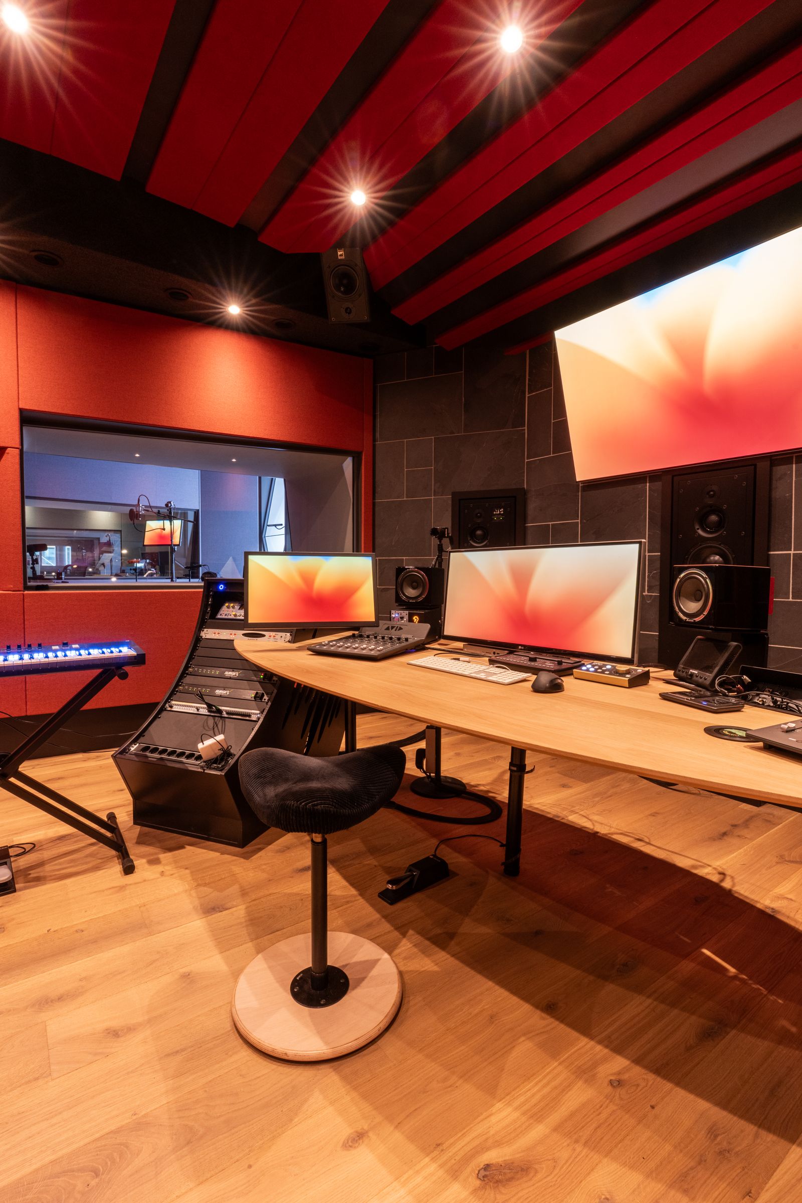 Studio van TFA met rode wanden, een houten regietafel, keyboard en studiomonitoren
